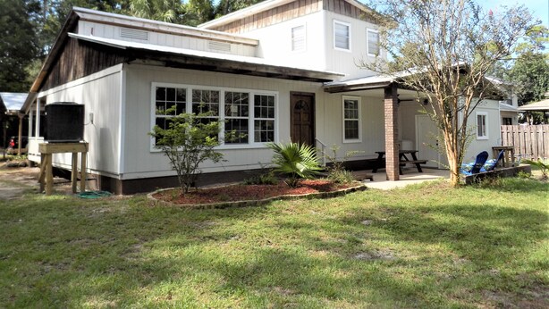 A two-story house with a covered porch, a small garden, and a wooden fence. - The Bay Cottage Adventure (Pensacola)