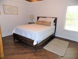 Une chambre à coucher avec un lit en bois, une table de chevet avec une lampe, un tapis à motifs et une fenêtre avec des stores.
