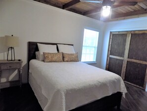 A bedroom with a bed, a nightstand, a lamp, a window, and a wooden door.
