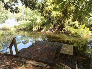 A wooden dock extending into a calm body of water surrounded by dense greenery.