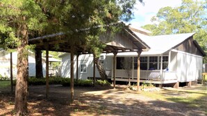 A wooden house with a porch and a covered area, surrounded by trees and a clear sky. - The Bay Cottage Adventure (Pensacola)