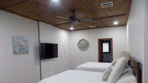 A bedroom with two beds, a ceiling fan, a TV, and a door. - The Bay Cottage Adventure (Pensacola)