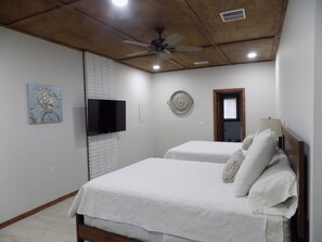 Una camera da letto con due letti, una ventola a soffitto, una televisione e una porta.