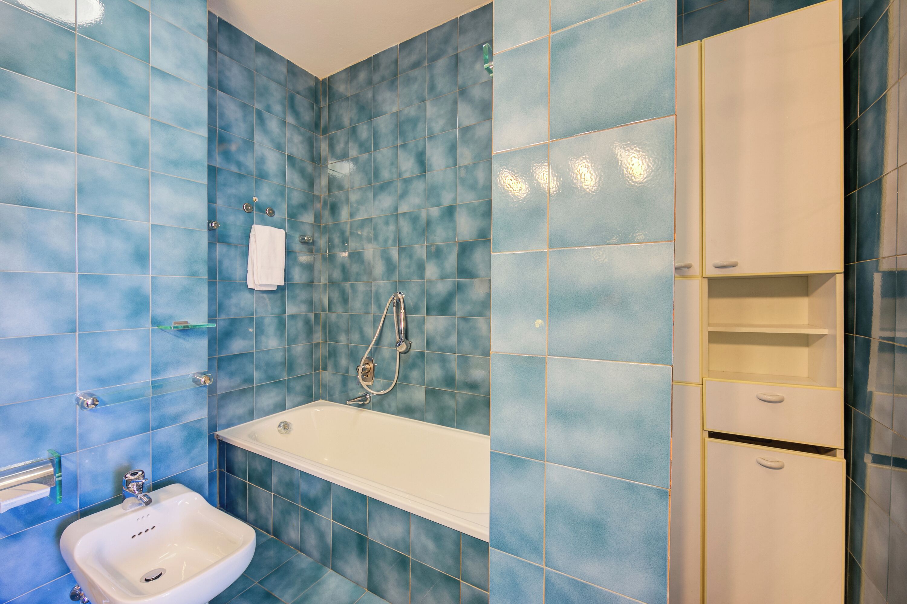 A bathroom with blue tiles, a white sink, a bathtub, and a cabinet.