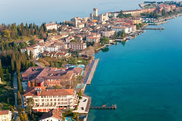 An aerial view of a coastal town with buildings along the waterfront, a marina, and a castle-like structure in the background.