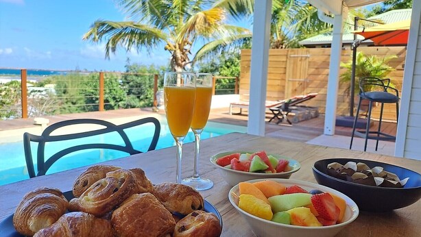 A table with croissants, fruit, and a drink, overlooking a pool and palm trees. - Villa Moringa Vue Mer - 5 mn Orient Bay or Grand Case (ST MARTIN)
