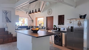 A modern kitchen with a central island, stainless steel appliances, pendant lighting, and a large clock on the wall. - Villa Moringa Vue Mer - 5 mn Orient Bay or Grand Case (ST MARTIN)