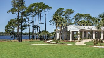 Enjoy serene lakeside views from the covered patio area, surrounded by tall pine and palm trees. at Bluegreens Bayside Resort and Spa