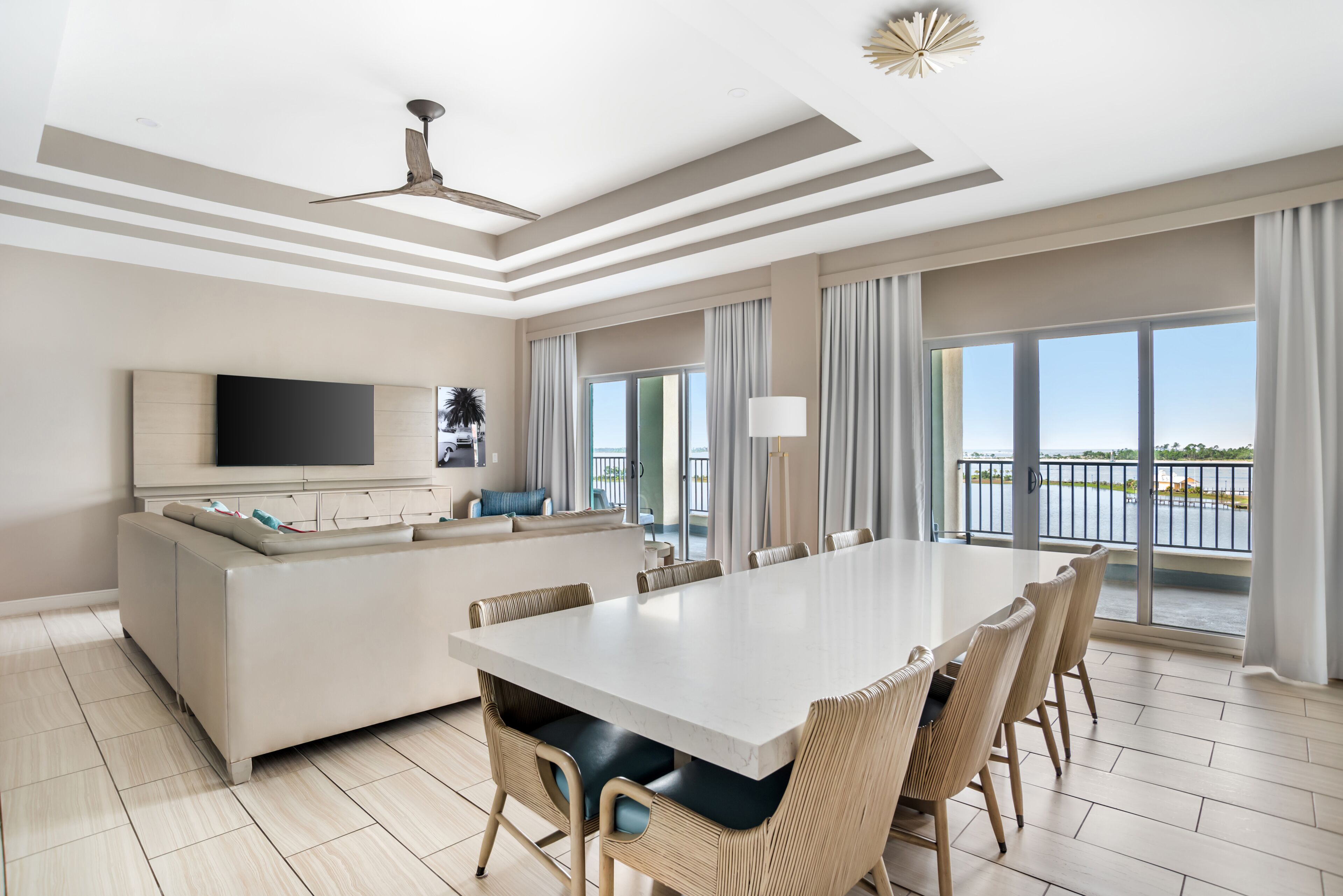 Een moderne hotelkamer met een ruime eettafel, een bank, een flatscreen televisie en een balkon met uitzicht op het water.
