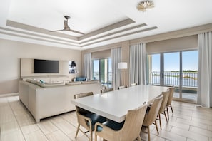 Een moderne hotelkamer met een ruime eettafel, een bank, een flatscreen televisie en een balkon met uitzicht op het water.