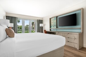 Ein Hotelzimmer mit einem großen Bett, einem Schreibtisch mit Flachbildfernseher und Blick auf Grünflächen.