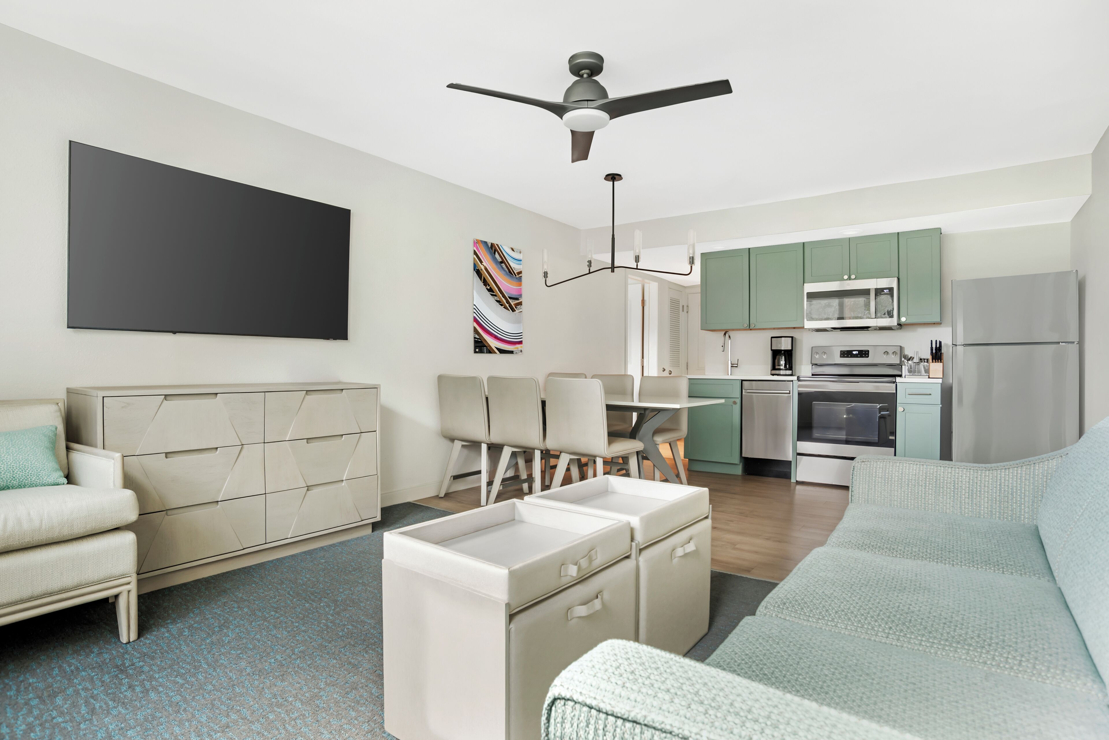 Una sala de estar moderna con un sofá, un comedor con sillas, una cocina con armarios verdes y un ventilador de techo.
