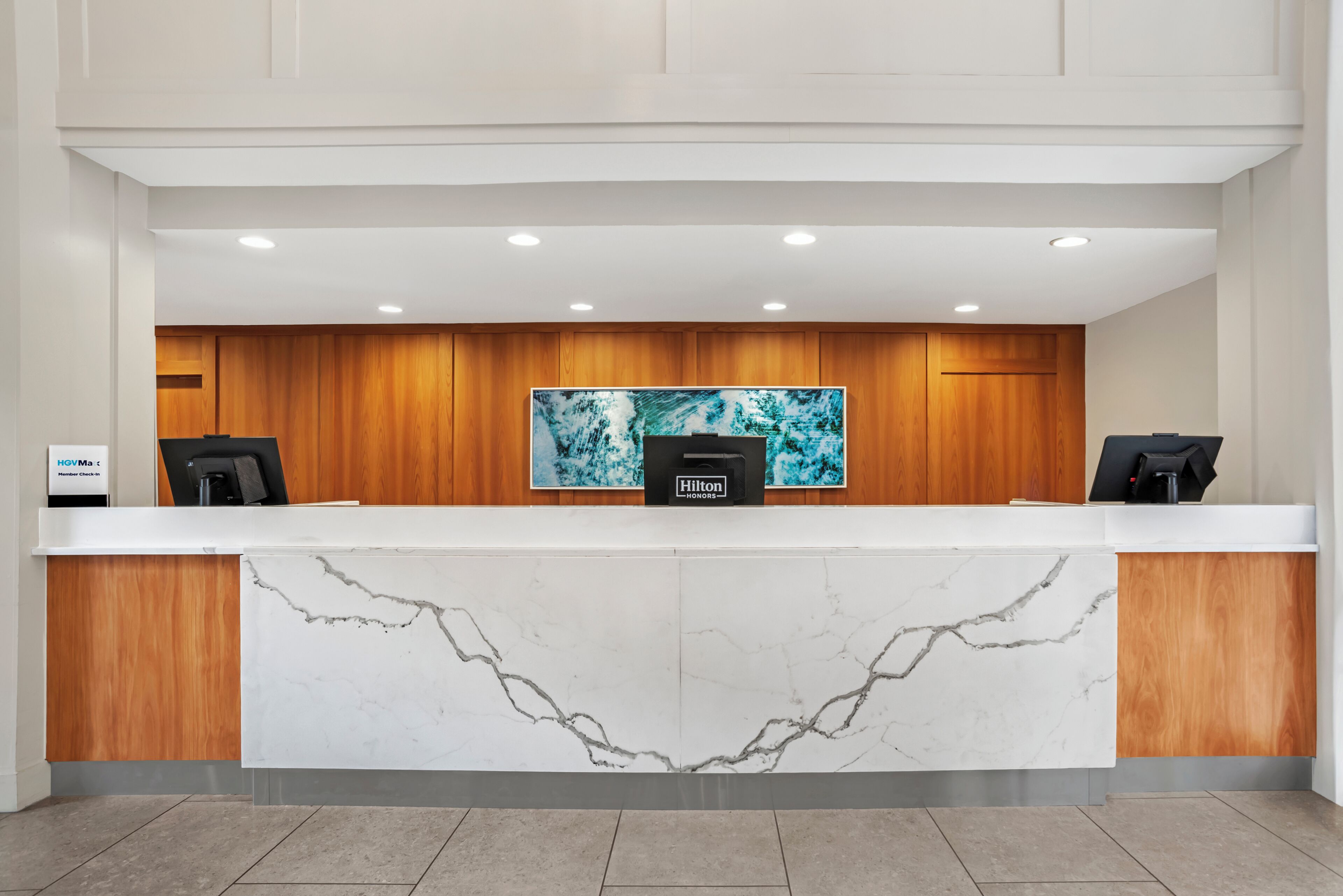 A hotel reception desk with a marble front, wooden paneling, and a large artwork above.