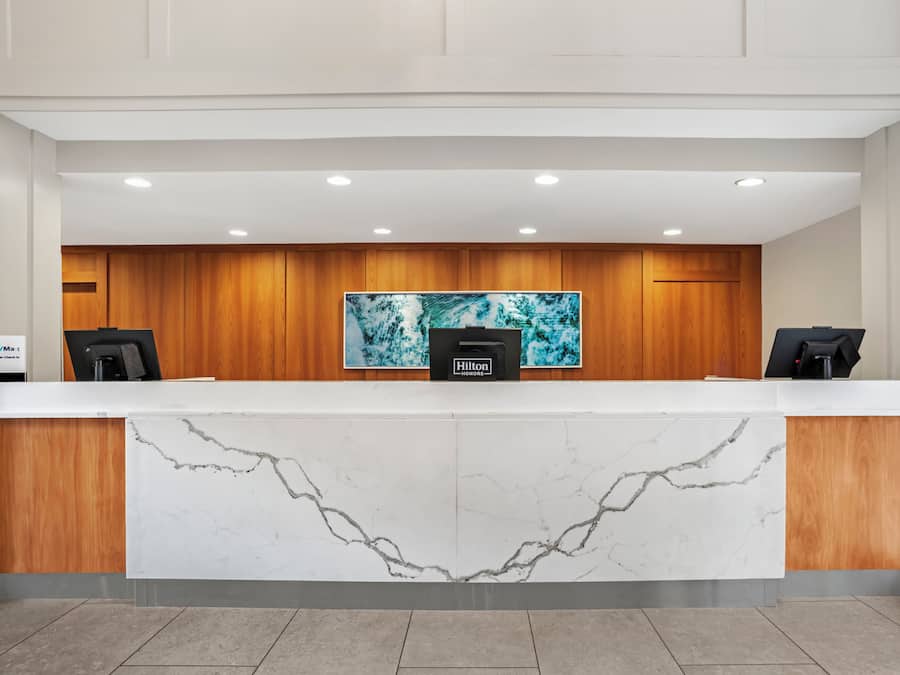 A hotel reception desk with a marble front, wooden paneling, and a large artwork above.