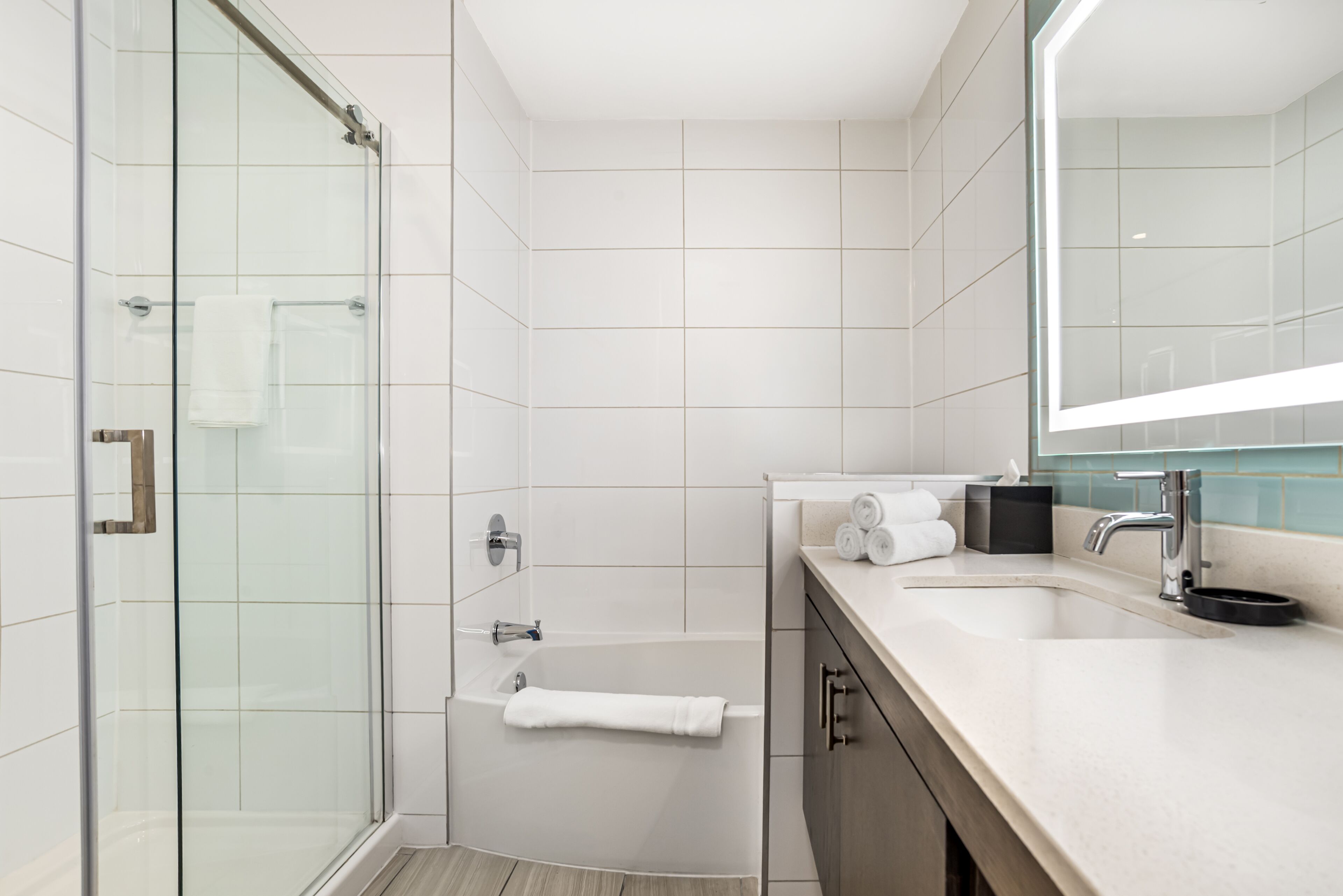 A modern bathroom with a glass shower enclosure, a bathtub, and a vanity with a mirror.