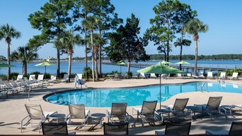 Relax by the pool surrounded by lounge chairs and umbrellas, with a wooden pier extending into the water. at Bluegreens Bayside Resort and Spa