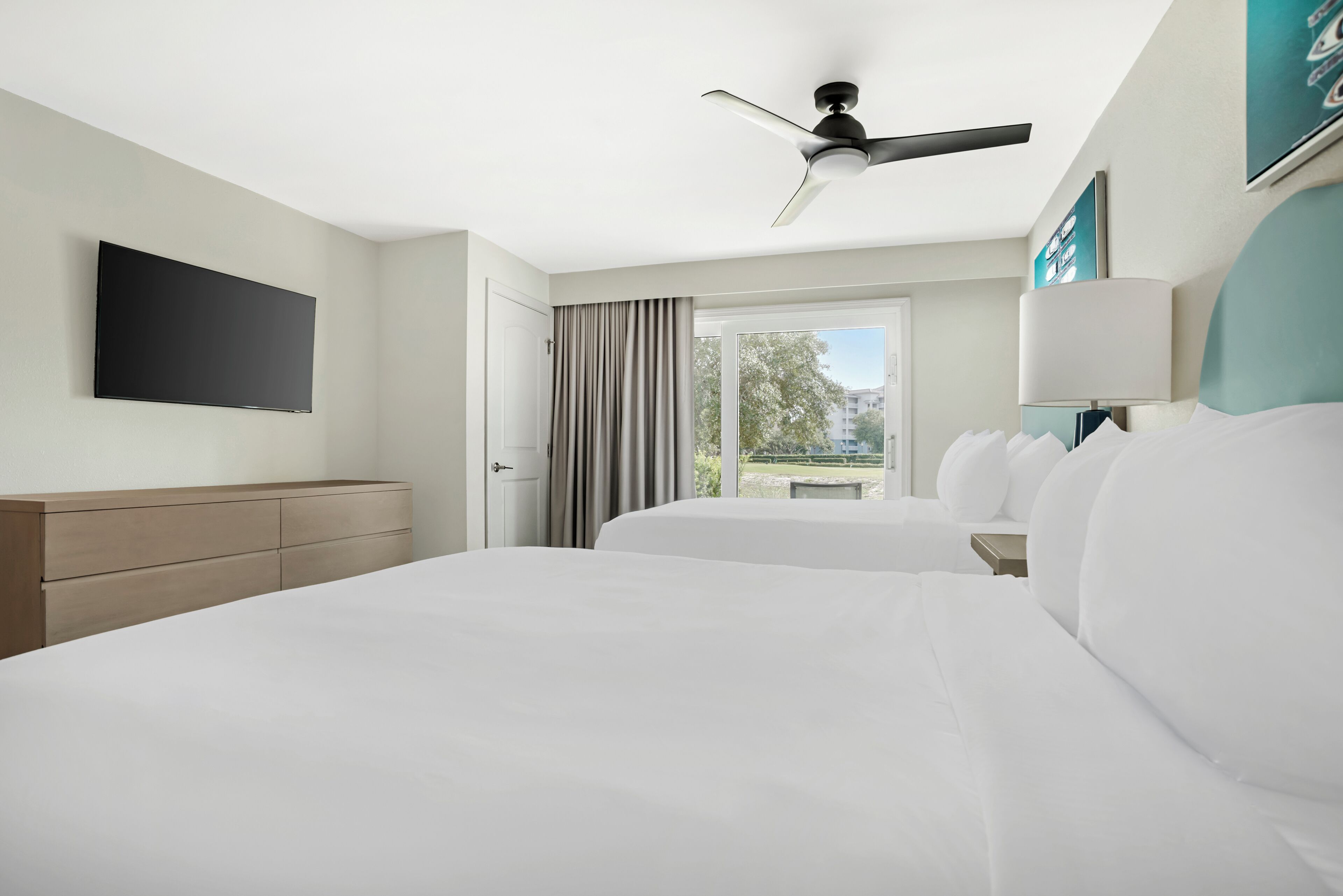 A hotel room with two beds, a flat-screen TV, a ceiling fan, and a window with curtains.
