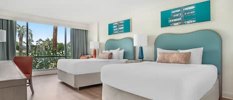 Habitación de hotel con dos camas, un escritorio y vistas a palmeras.