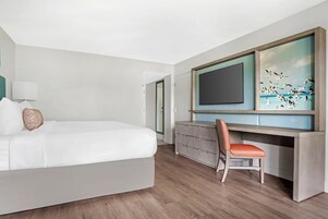 Quarto de hotel moderno com uma cama grande, uma escrivaninha com cadeira, televisão de tela plana e vista para o mar.