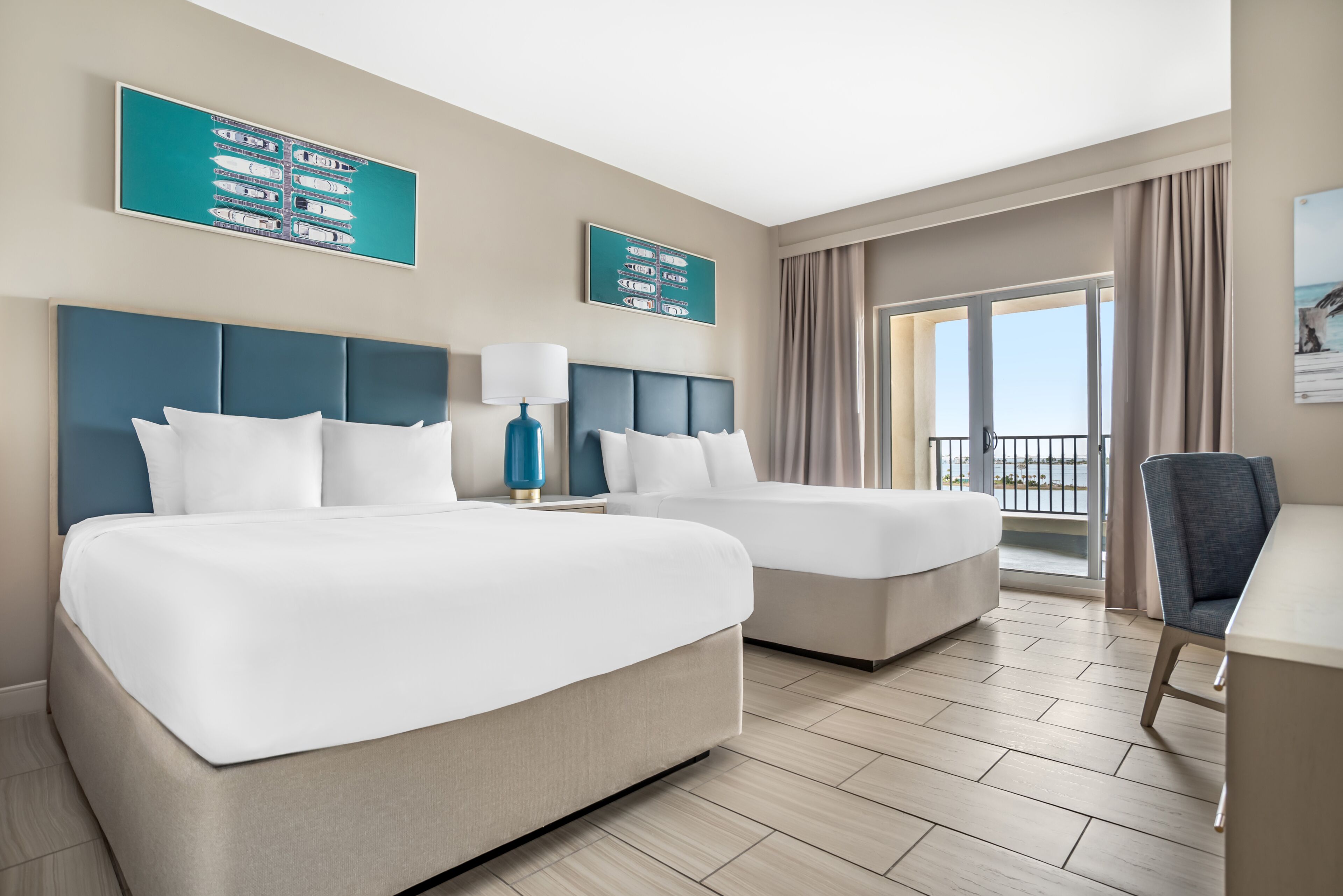 A hotel room with two beds, a desk, a chair, and a balcony with a view.