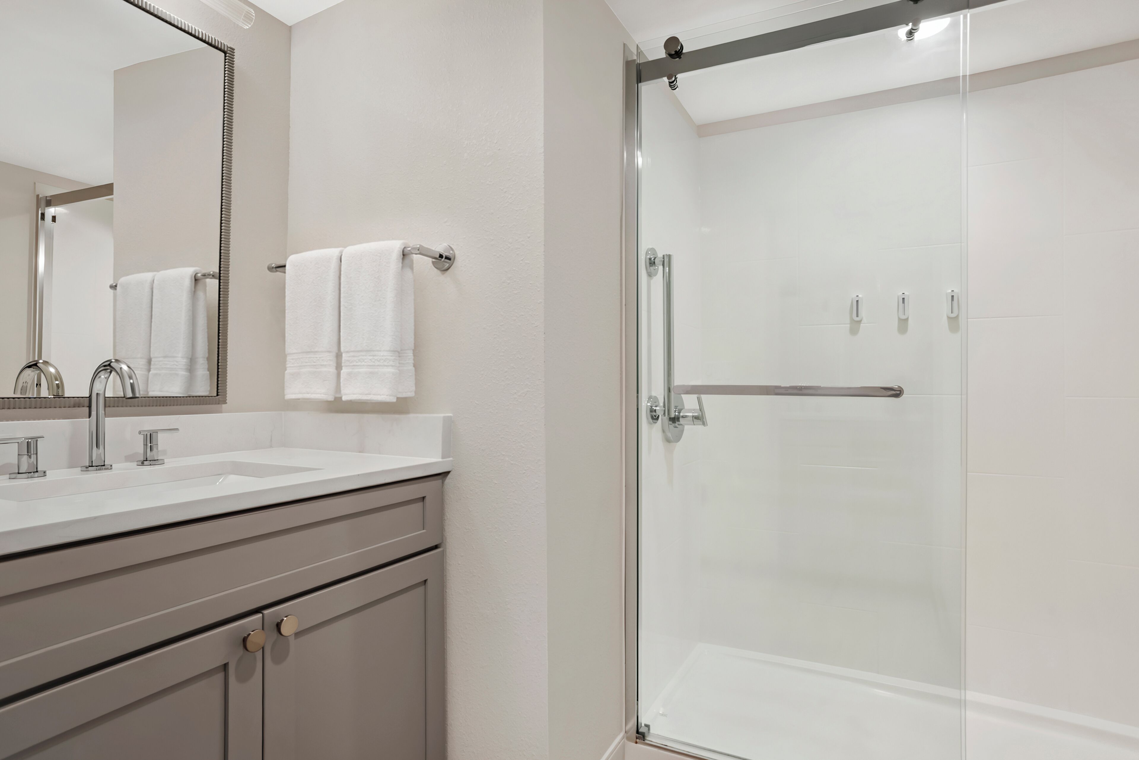 Un baño con cabina de ducha de vidrio, un lavamanos con espejo y un perchero para toallas.