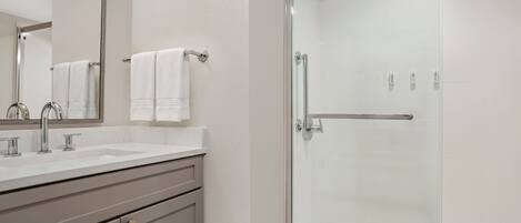 Un baño con cabina de ducha de vidrio, un lavamanos con espejo y un perchero para toallas.
