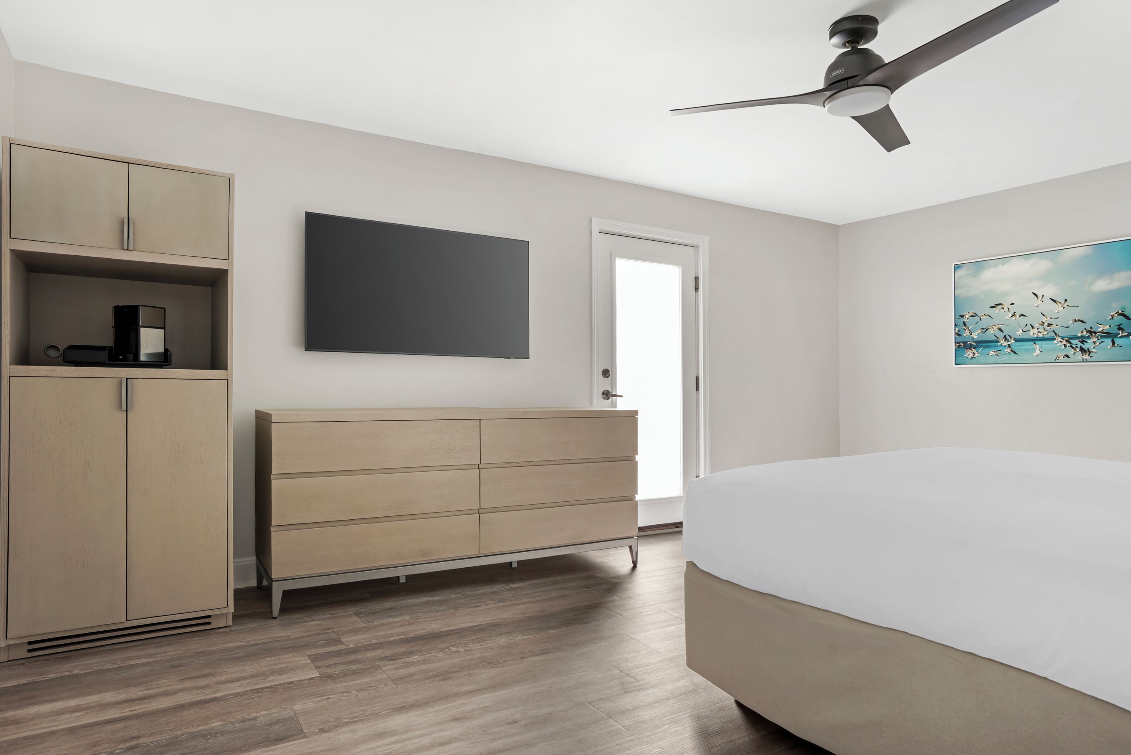 A bedroom with a bed, a wardrobe, a flat-screen TV, a ceiling fan, and a painting on the wall.