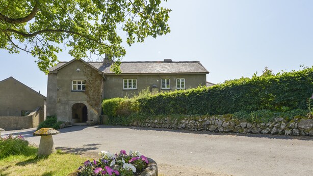 A stone building with a paved driveway and a flower bed in the foreground.