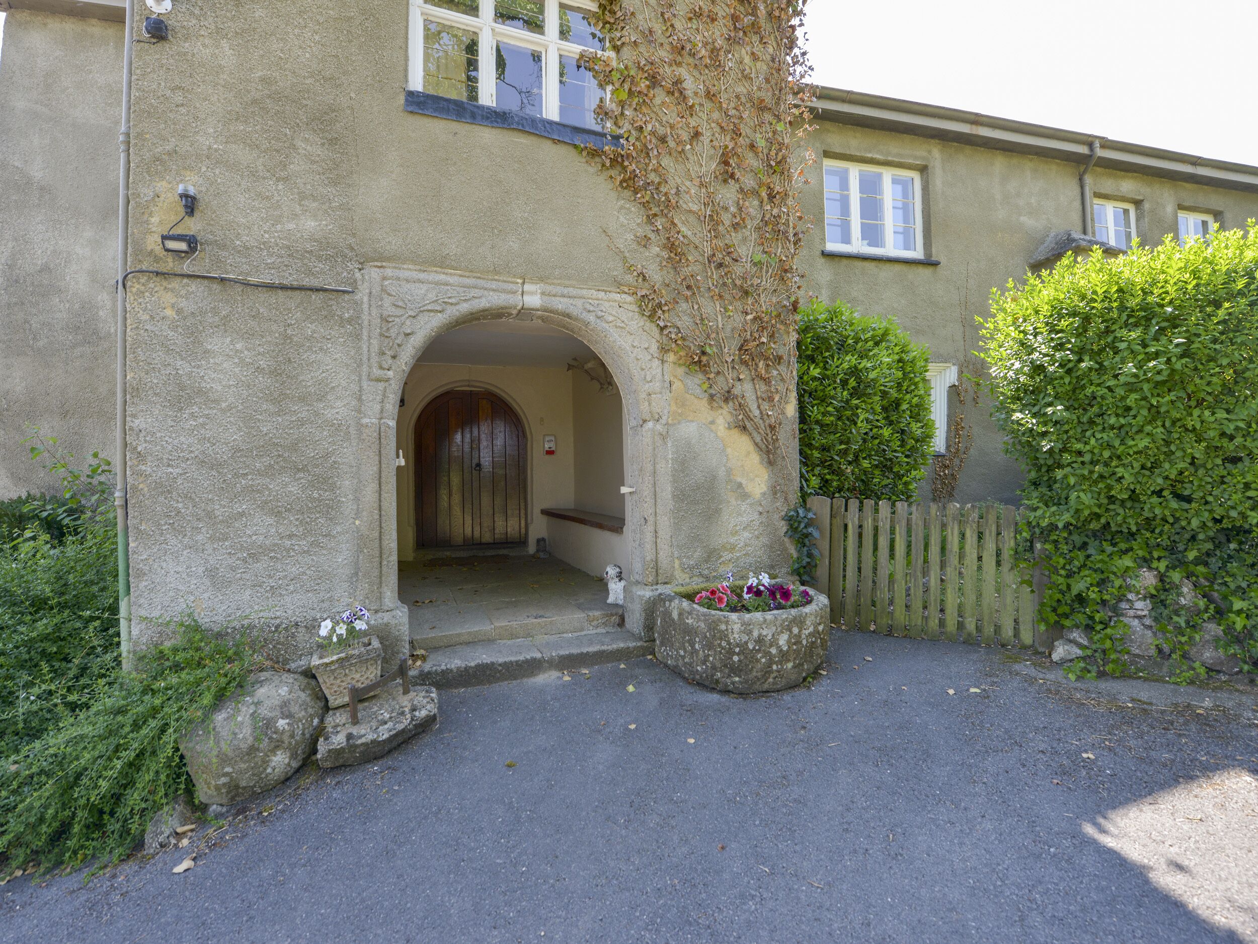 A stone building with an arched entrance, a wooden door, and a small porch area with potted plants.