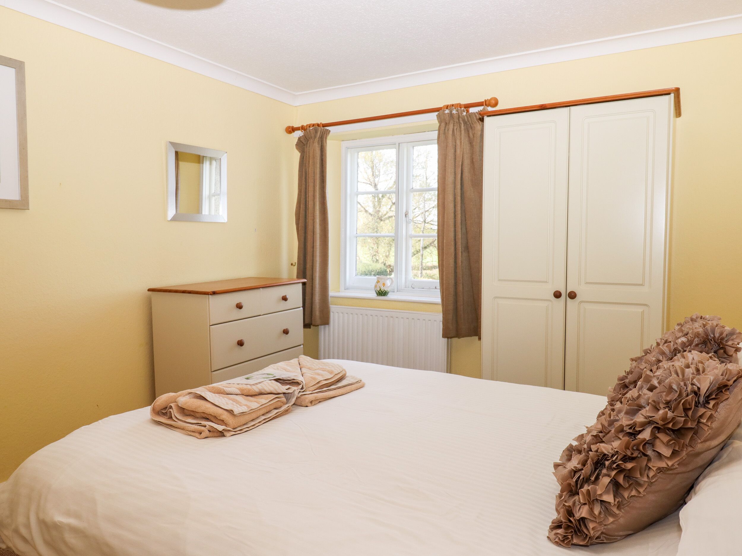 Une chambre à coucher avec un lit, une commode, une fenêtre avec des rideaux et une porte.