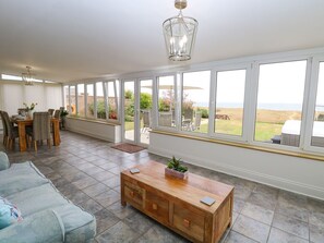 A spacious living area with a large window, a wooden coffee table, a sofa, and a dining table with chairs. - Drifters (Great Yarmouth)