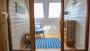 Ett rum med trägolv, en blårandig matta, en blå stol, ett träskåp och en tavla på väggen.