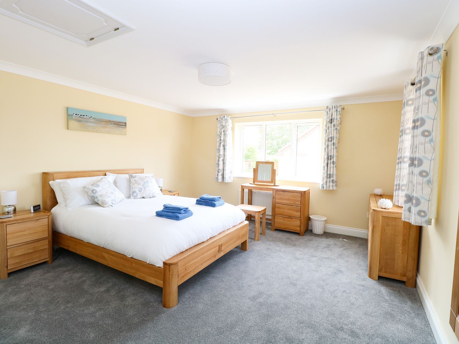 A neatly arranged bedroom with a wooden bed, a desk, and a chair, a radiator, and a window with curtains.