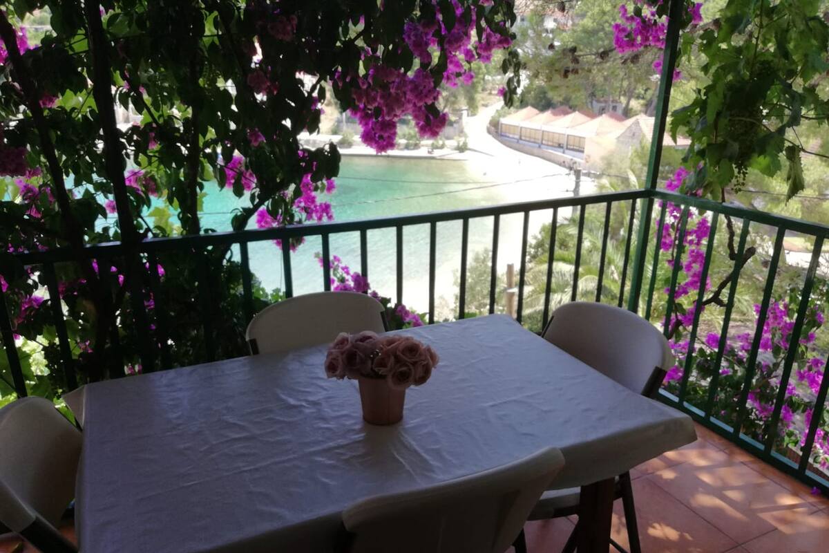 Ein Balkon mit Tisch und Stühlen, mit Blick auf ein Gewässer und Grünflächen.
