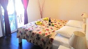 Ein Hotelzimmer mit Bett, einem Fenster mit Vorhängen, einem Nachttisch mit Lampe und einem kleinen Tisch mit Flasche und Gläsern.