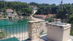 Eine Terrasse mit Steinbalustrade und grüner Metallgeländer, mit Blick auf ein Gewässer und eine Hügellandschaft mit Gebäuden.