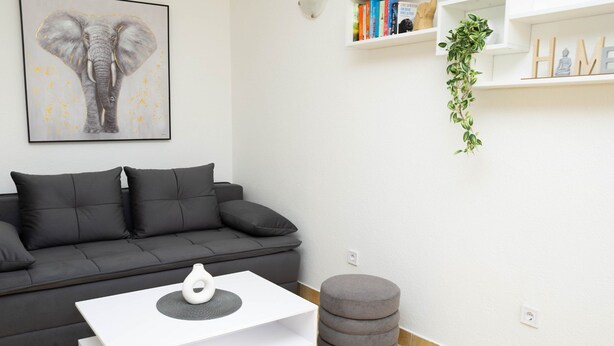 A modern living room with a grey sofa, a white coffee table, and a grey ottoman. - Apartment Olga (Dubrovnik)