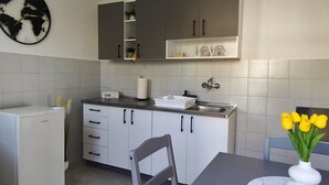 A modern kitchen with grey cabinets, a white refrigerator, a sink, and a vase with yellow flowers on the table. - Apartment Olga (Dubrovnik)