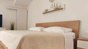A bedroom with a bed, bedside table, and a wall-mounted shelf with decorative items. - Apartment Olga (Dubrovnik)