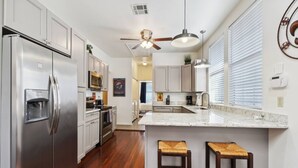 A modern kitchen with stainless steel appliances, a granite countertop, wooden stools, and a ceiling fan. - 3 Bedroom Home in the Heart of New Orleans! (New Orleans)