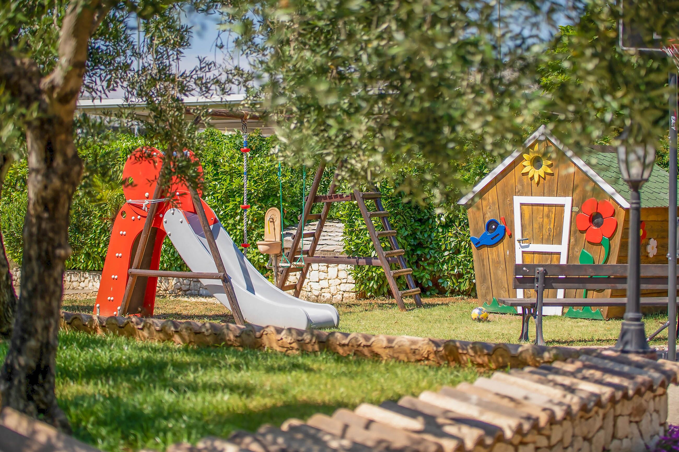 A playground with a slide, a wooden playhouse, and a bench.