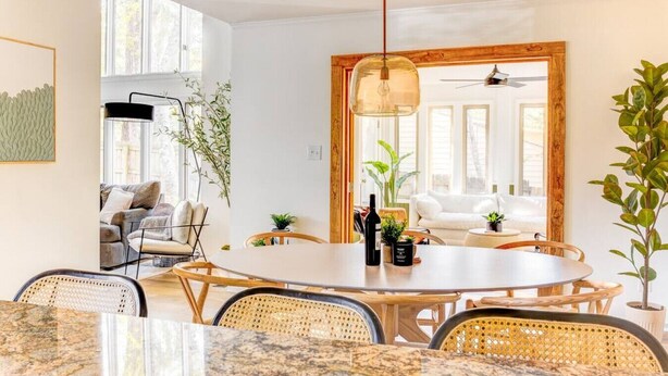 A modern dining area with a round table, wicker chairs, and a hanging light fixture.