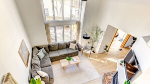 A spacious living room with a large window, a sectional sofa, a coffee table, and a stone fireplace.