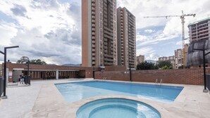 A swimming pool area with a hot tub, surrounded by a brick wall and a tall building in the background. - 3 Bed 2.5 Bath Modern Apartment in Laureles (Medellín)