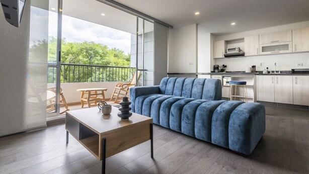 A modern living room with a sofa, a table, and a balcony with a view of greenery. - 3 Bed 2.5 Bath Modern Apartment in Laureles (Medellín)