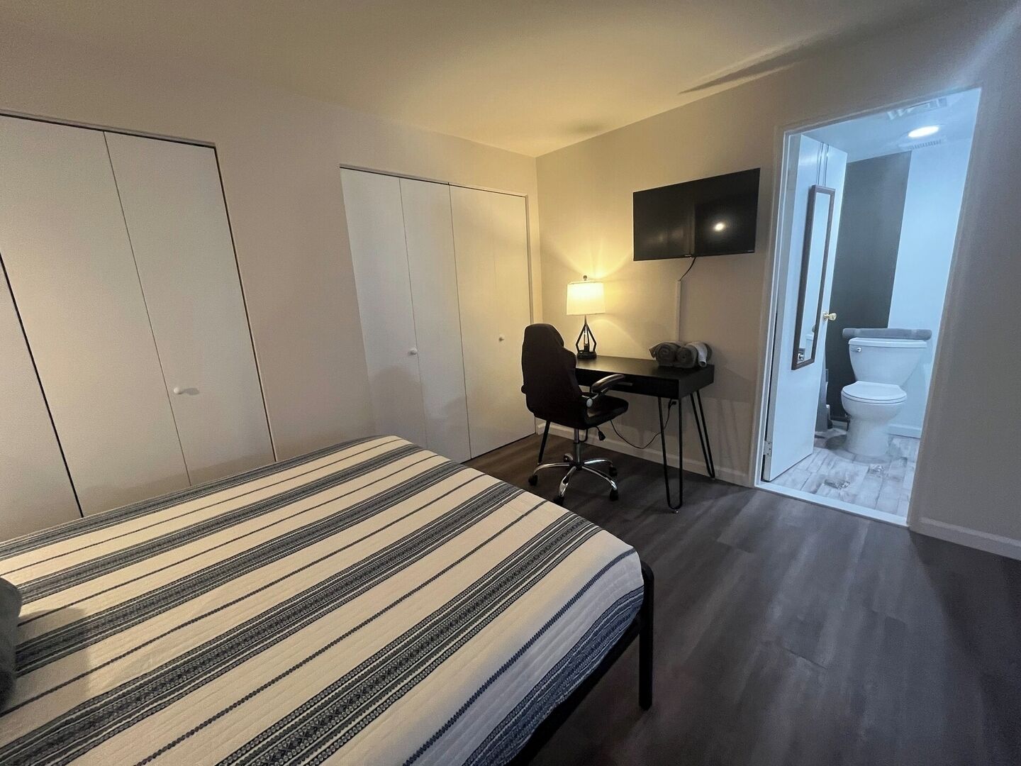 Ett sovrum med en säng, ett skrivbord, en stol, en tv och ett badrum.