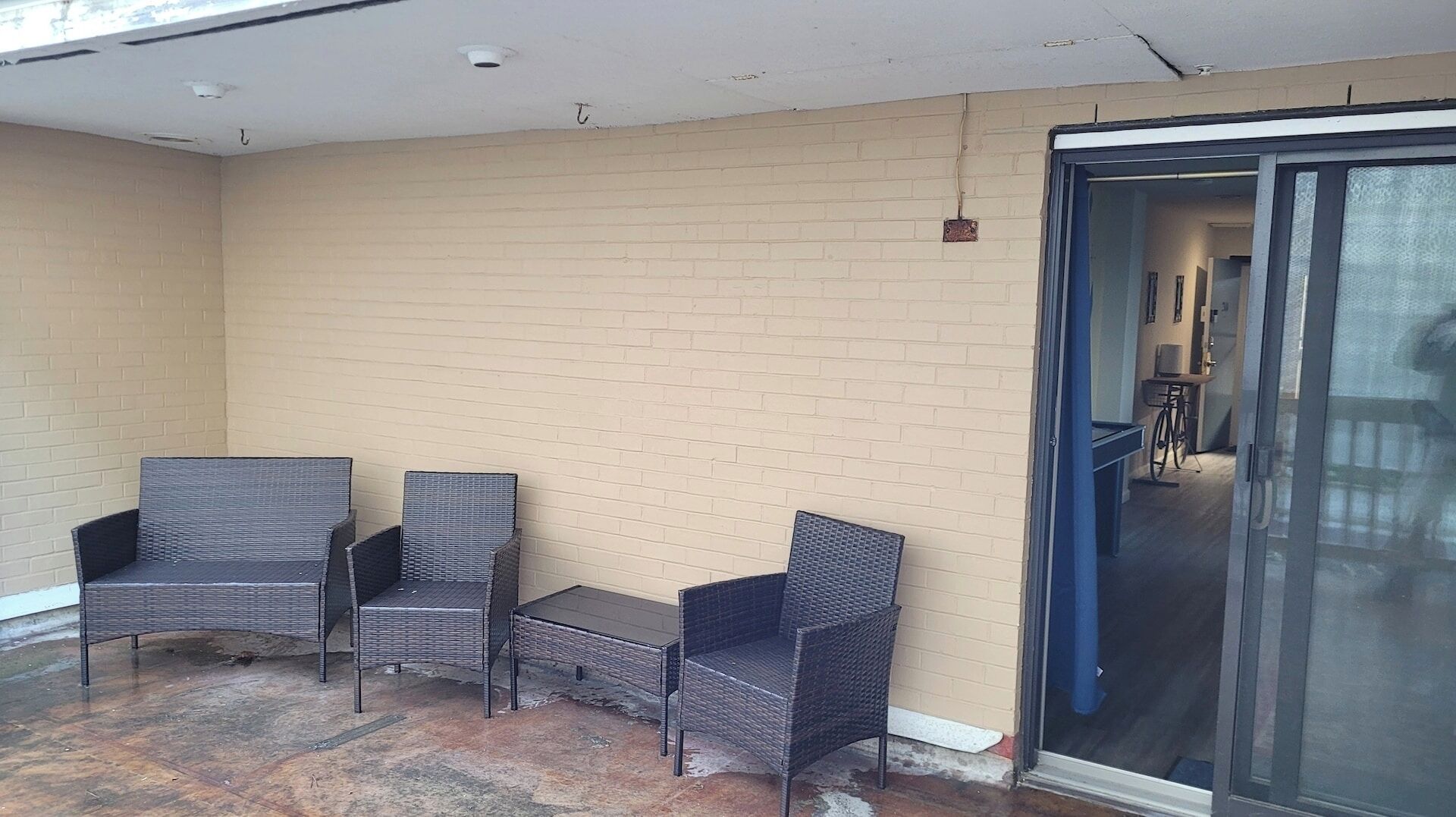An outdoor seating area with wicker chairs and a small table, a sliding glass door, and a brick wall.