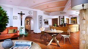 A hotel lobby with a reception desk, a reception area, a wooden coffee table, a sofa, and a chandelier. - Medrazerhof (Fulpmes)