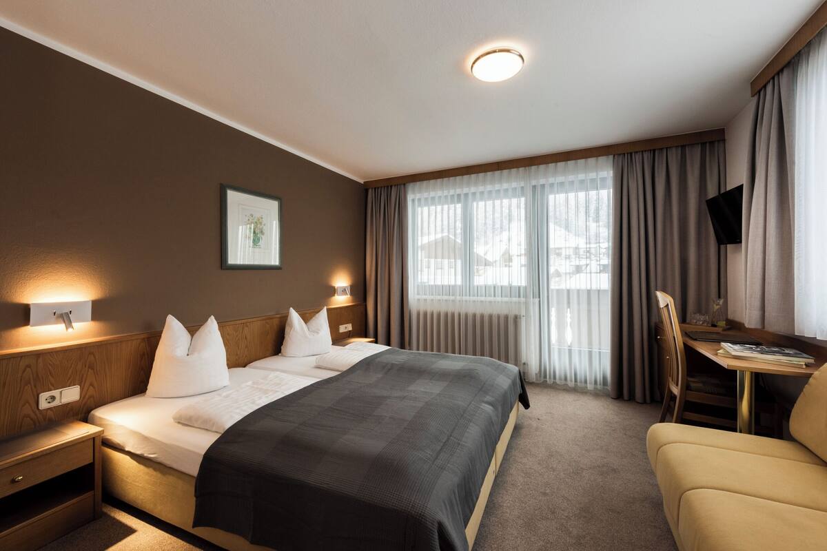 A hotel room with a large bed, bedside tables, a desk, a chair, and a television.