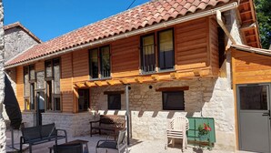Ein Holzhaus mit Ziegeldach, Steinmauern und einer überdachten Veranda mit Gartenmöbeln.